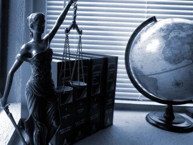 En lady justice statue med bøker og en jordklode på et skrivebord med persienner trekt for vinduet i bakgrunnen