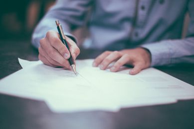 En person i blå skjorte som sitter ved et skrivebord og skriver under noen dokumenter