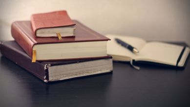 Flere lærbundede bøker som ligger oppå hverandre med en åpen notatbok i bakgrunnen med en penn som ligger på en av sidene