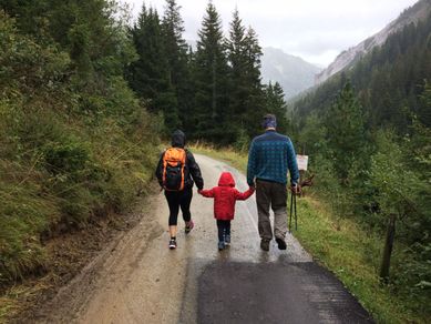 En mann og en kvinne som går på tur på en grusvei med en barn mellom seg som holder begge to sine hender på fjellet på en grå dag